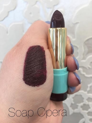 Bold Colours, a hand with a lipstick swatch holding a deep wine-plum lipstick