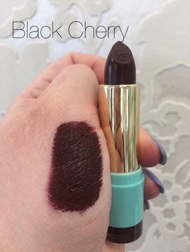 Bold Colours, a hand with a lipstick swatch holding a deep wine-plum lipstick
